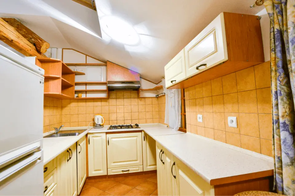 Kuchnia z jasno beżowymi meblami, umywalką, czajnikiem oraz dwoma gniazdkami