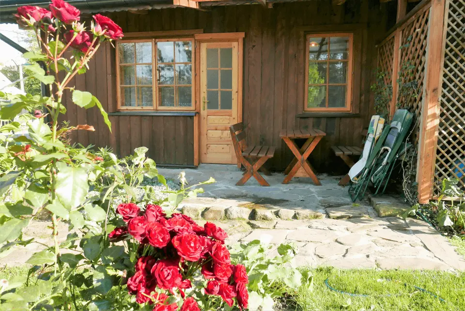 Czerwone kwiaty oraz wejście do apratamentu pod jodełką, przed wejściem znajduje się stolik z dwiema ławkami