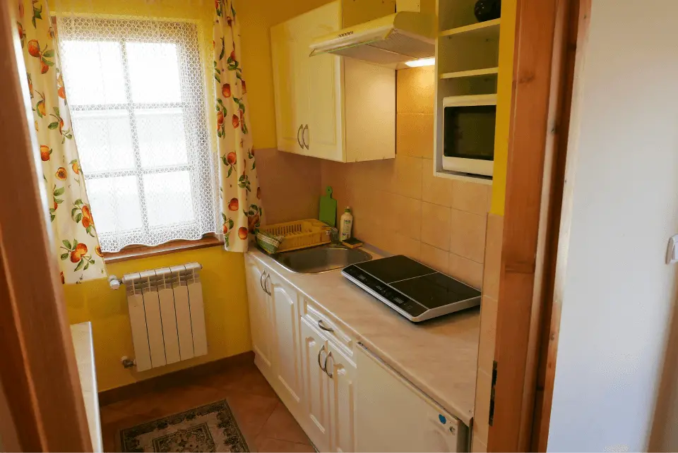 Kuchnia z płytą grzewczą, lodówką, okapem oraz oknem i grzejnikiem