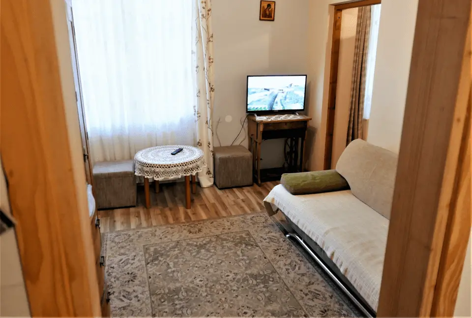 Pokój ze stolikiem, dwiema pufami, łóżkiem oraz włączonym telewizorem